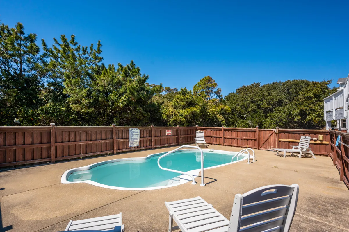 This image showcases a sparkling swimming pool surrounded by lush greenery, with inviting poolside chairs arranged for relaxation. The tranquil setting highlights the pool as the centerpiece of the yard, suggesting a space perfect for swimming, sunbathing, and leisurely afternoons outdoors.