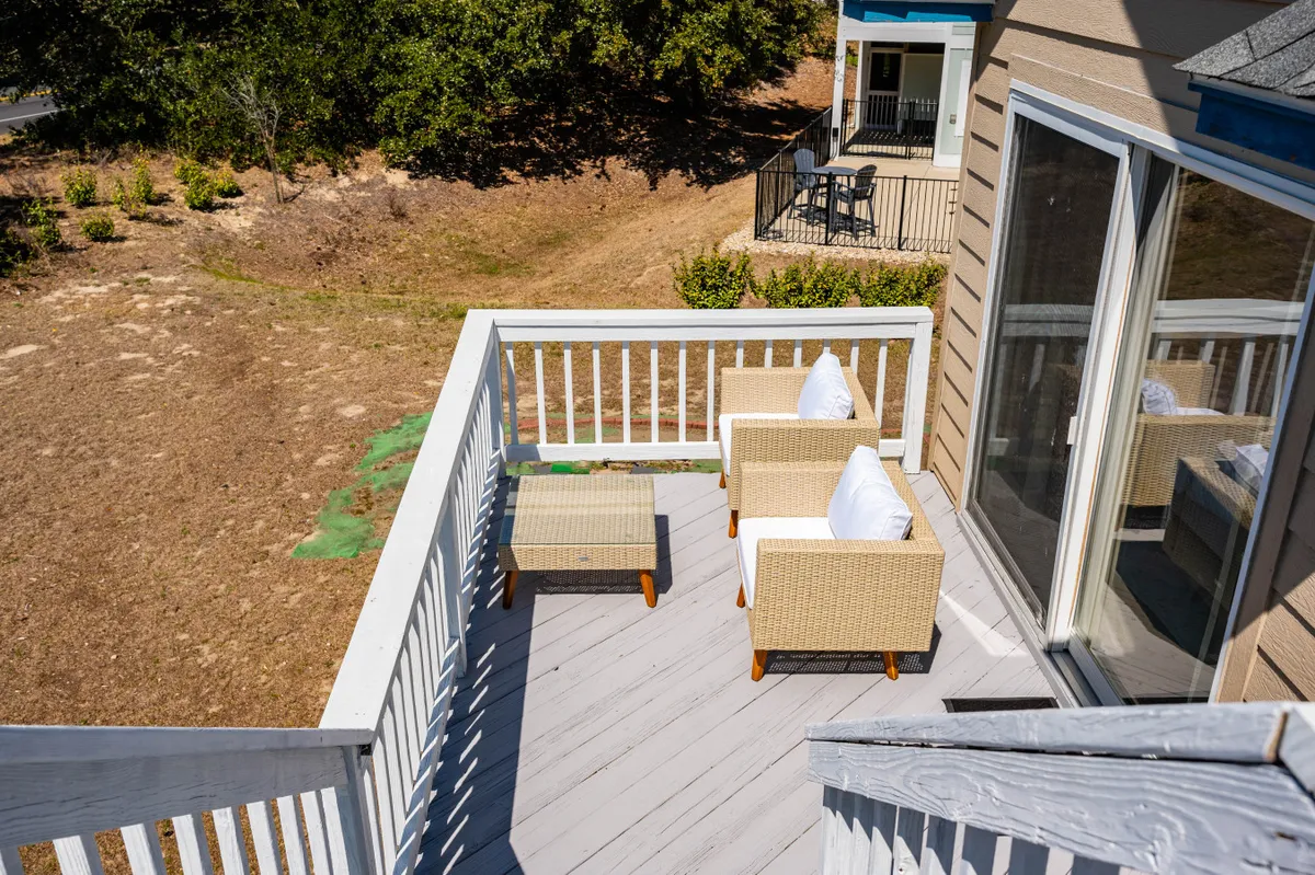 This image shows a welcoming exterior deck area with comfortable outdoor seating, surrounded by lush greenery and railings. The space invites guests to relax, socialize, or enjoy morning coffee while being sheltered from the elements. The atmosphere is serene and friendly, making it an ideal spot for gathering when indoor activities are preferred due to weather.