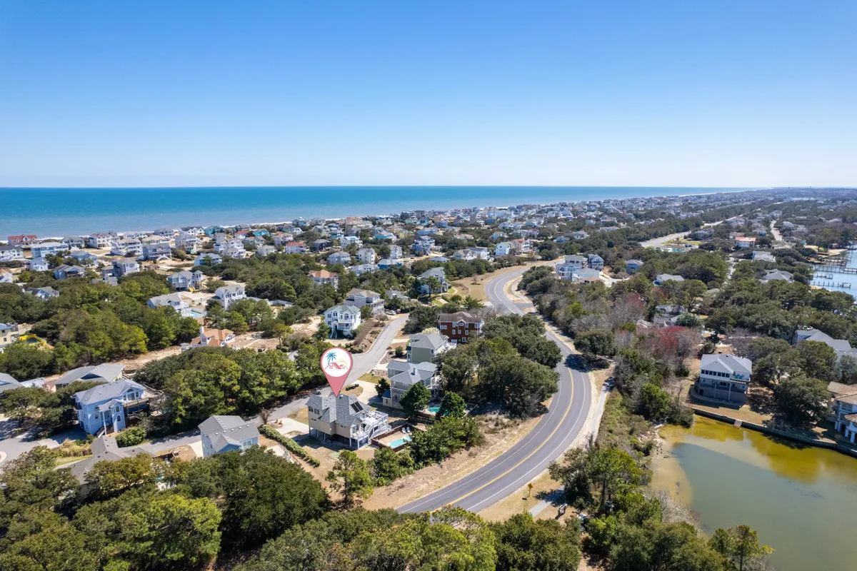 This image showcases a sweeping view of the ocean, a residential area, a curving road, vibrant greenery, and a pond. The natural landscape is rich and inviting, with visible opportunities for wildlife sightings and nature walks.