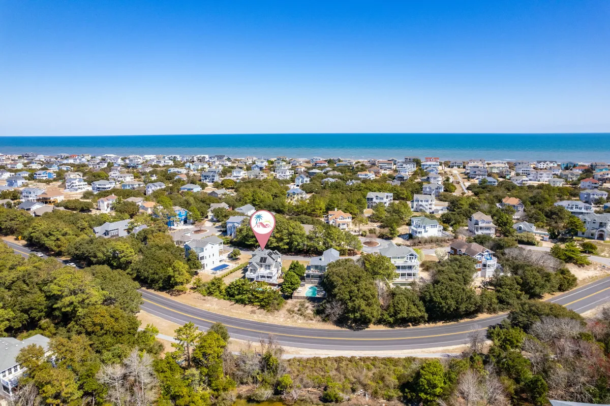 A wide exterior shot featuring a sweeping ocean view, parts of the neighborhood layout, and a hot air balloon in the sky. Visible beach activity areas and groups suggest community gatherings and fun outdoor events, all set in a relaxed and cheerful coastal mood.