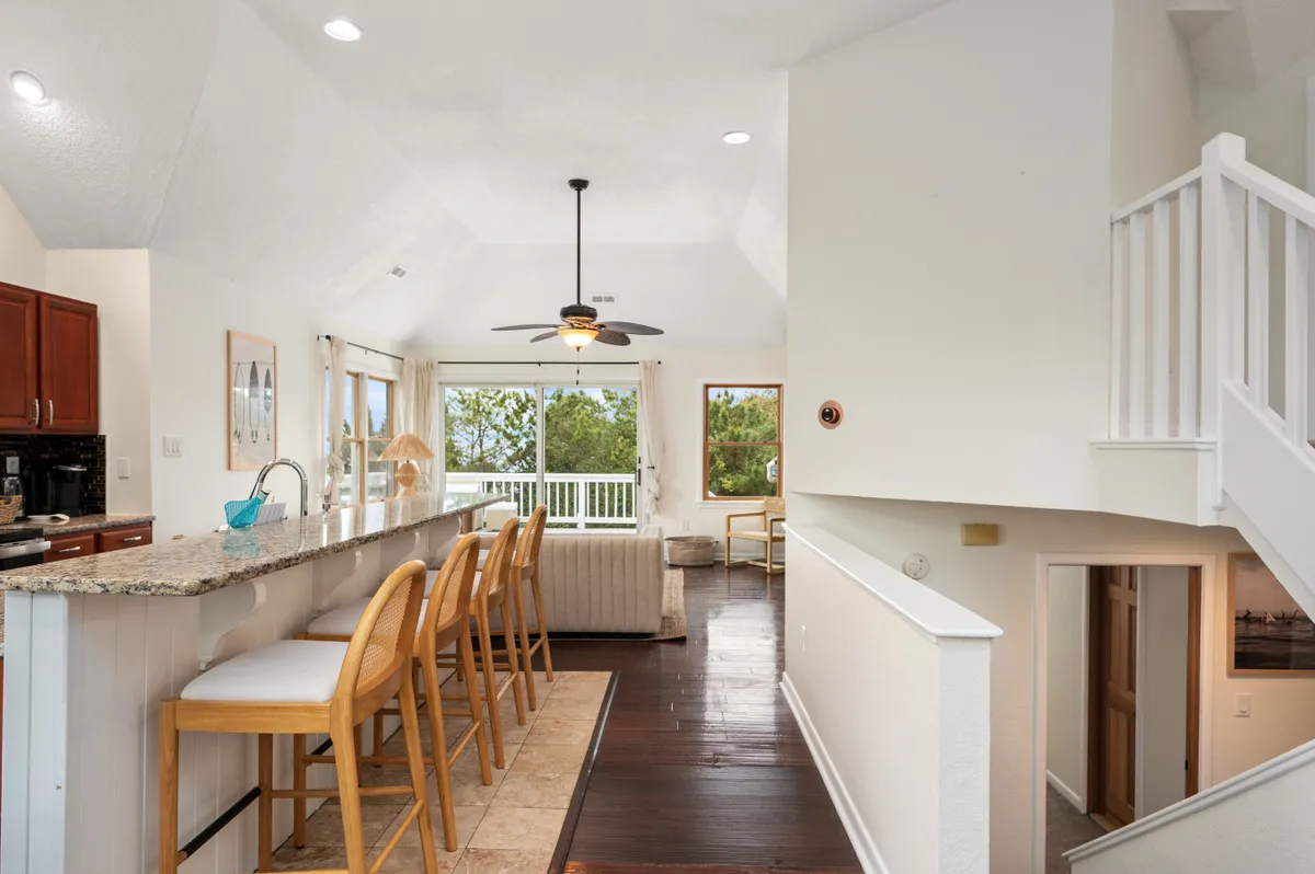 A spacious, open-plan interior integrating the kitchen and living room. The scene features a kitchen island with bar stools and a comfortable living area with ample seating, all illuminated by large windows. The layout encourages relaxation and socializing, ideal for group activities.