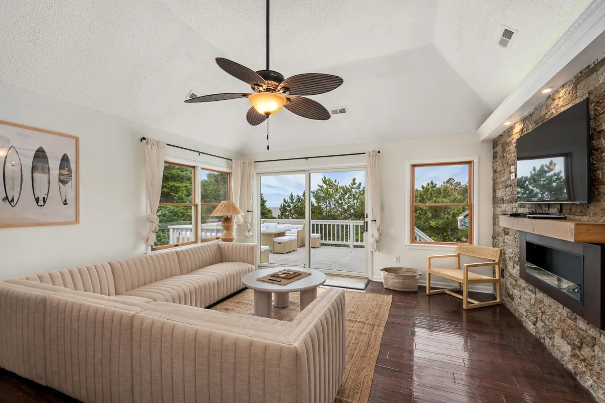 This interior image features a comfortable living room with a plush sofa, a coffee table ready for board games, a TV for movie nights, a stone wall adding warmth and character, and a view through glass doors. The space is inviting, ideal for group gatherings, playing games, or cozying up by the fireplace.