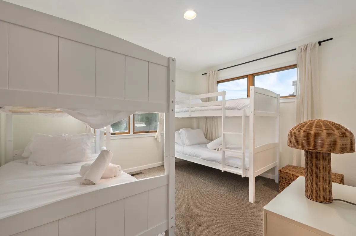 A cozy and playful bunk room designed for children, with two sets of bunk beds positioned by bright windows. A decorative lamp adds warmth and the space feels inviting yet fun, perfect for bedtime routines or late-night storytelling.