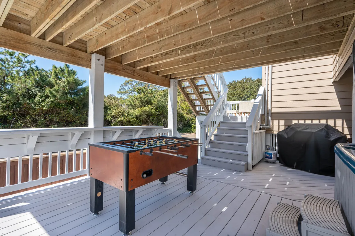 An exterior area featuring a foosball table, staircase, and grill set against the backdrop of an inviting outdoor space. It suggests social activities and family fun during evenings or when the weather is less favorable for outdoor exploration.