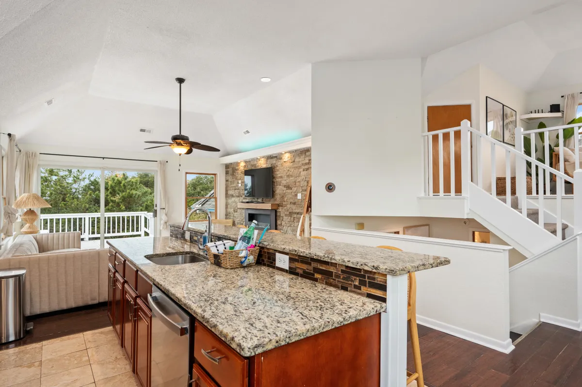 A spacious kitchen with a granite island serves as the centerpiece, complemented by a dramatic stone feature wall and large windows that fill the room with natural light. The kitchen is fully equipped, featuring modern appliances, and the open design connects seamlessly with the surrounding living space, inviting group cooking and interaction.
