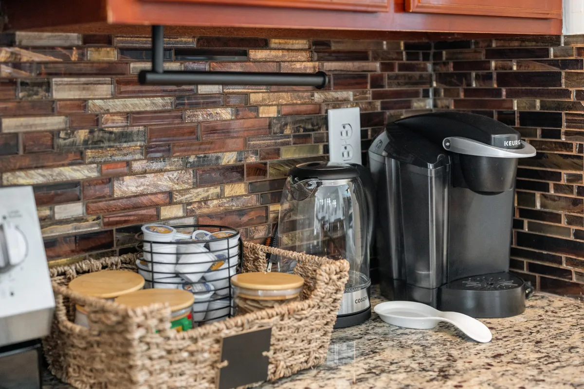 This close-up interior shot highlights a modern coffee maker, glass kettle, and a basket of jars on the kitchen counter. It emphasizes the convenience and warmth of having complimentary coffee and tea available, as mentioned in the section. The scene radiates homely comfort and hospitality.