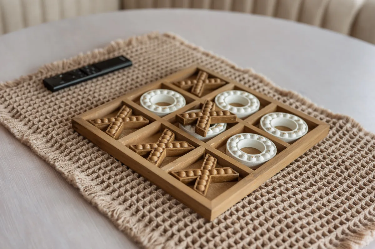 A close-up of a playful tic-tac-toe game on a coffee table, accompanied by a remote control and woven placemat. The arrangement evokes a cozy, inviting mood and emphasizes fun leisure time spent indoors.
